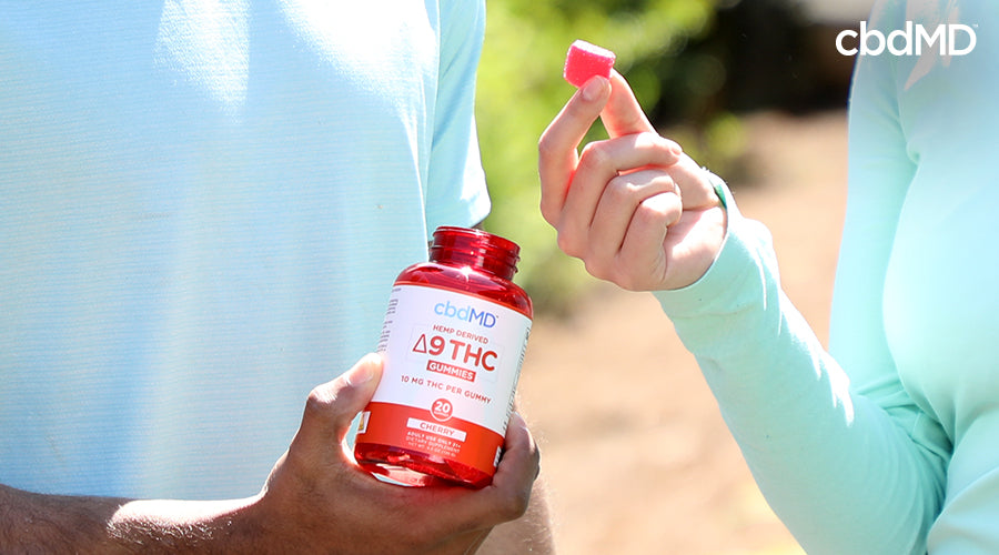 Someone holding a bottle of hemp derived delta 9 thc gummies cherry with someone else taking a gummy from the bottle - cbdMD