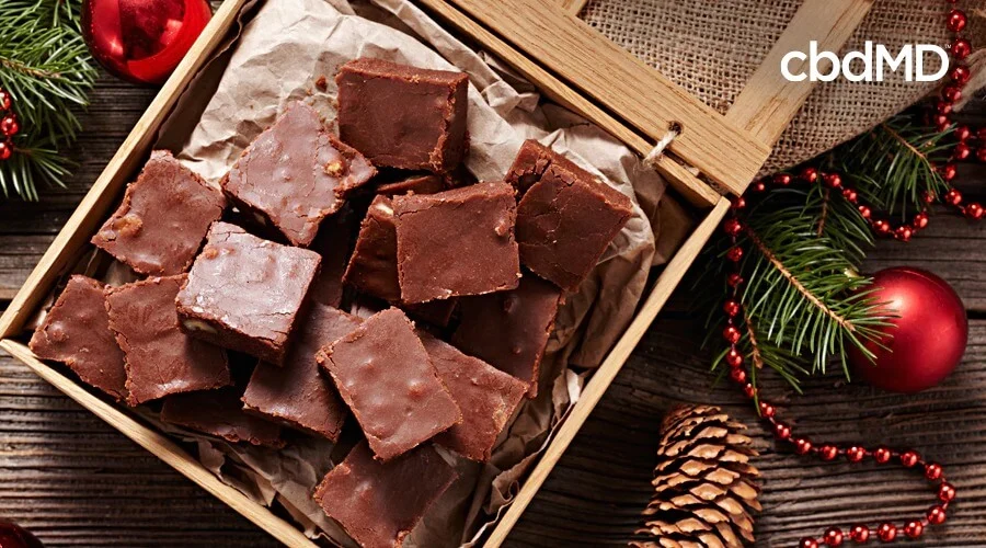 A box of holiday fudge sits among holiday decorations on a wooden table