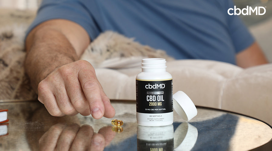 A man laying bed reaching for softgels from a bottle of full spectrum cbd oil softgels - cbdMD