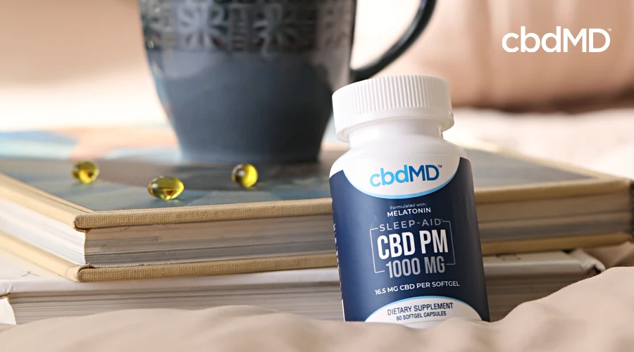 A bottle of cbd pm softgels sits on a bedside table next to a lamp