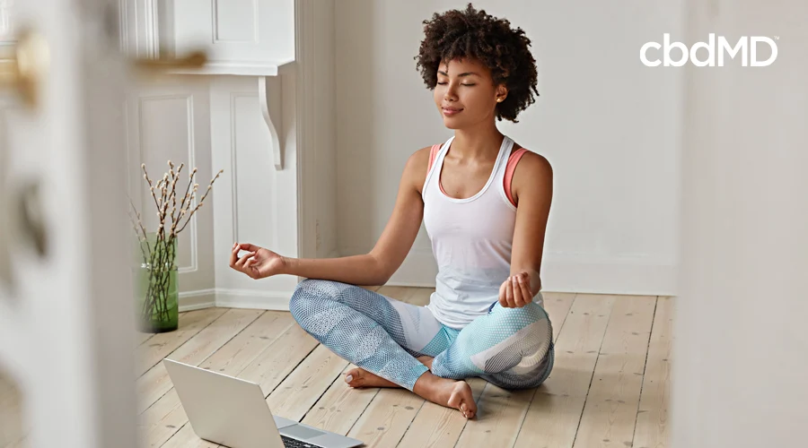 An attractive dark skinned woman sits crosslegged in meditation in her living room