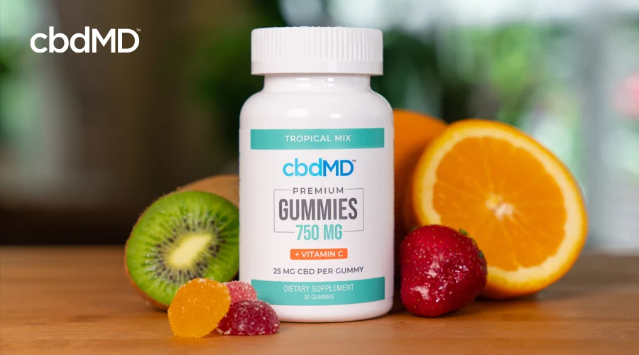 A bottle of 750 mg cbdMD CBD Gummies sits on a wooden table among assorted fruit