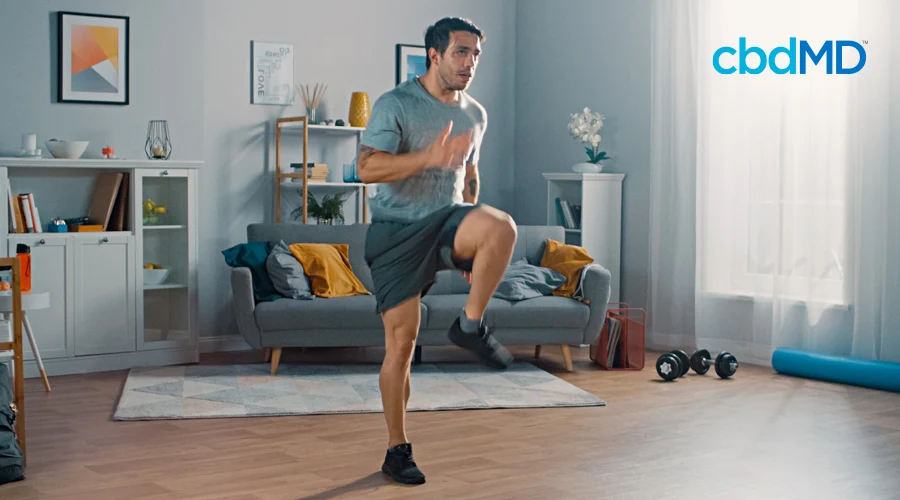 A dark haired man in exercise clothes runs in place in his living room