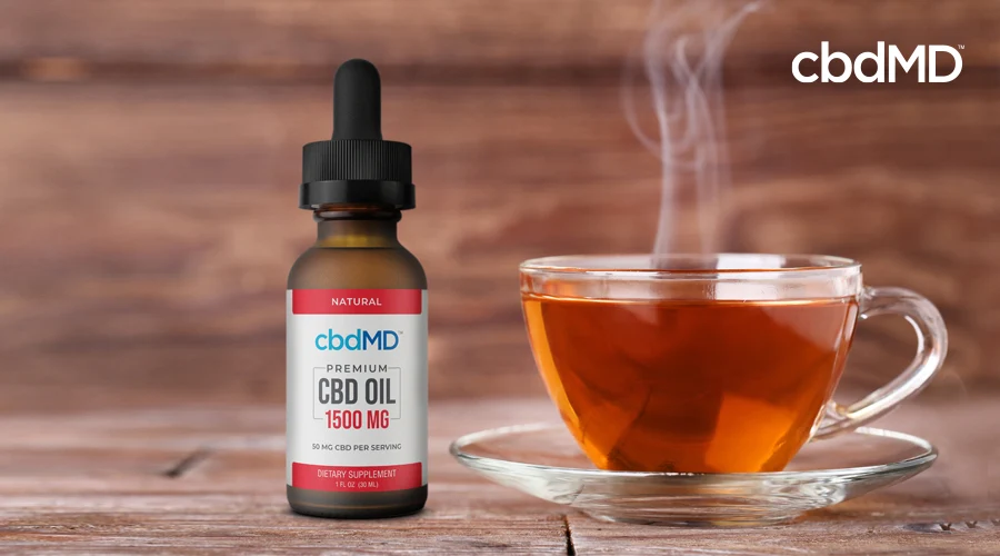 A bottle of 1500 mg cbd oil tincture from cbdmd sits next to a clear cup full of hot tea