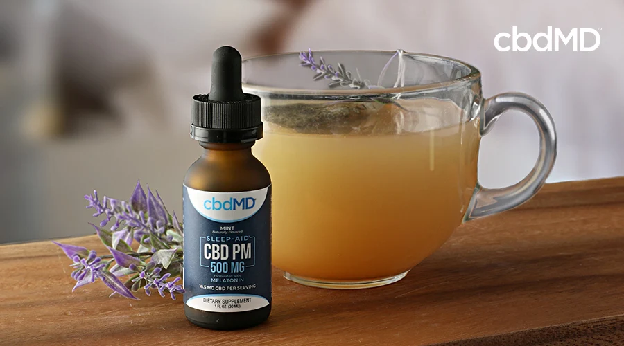 A delicious looking cup of tea with herbal garnish sits next to a bottle of cbd pm from cbdmd