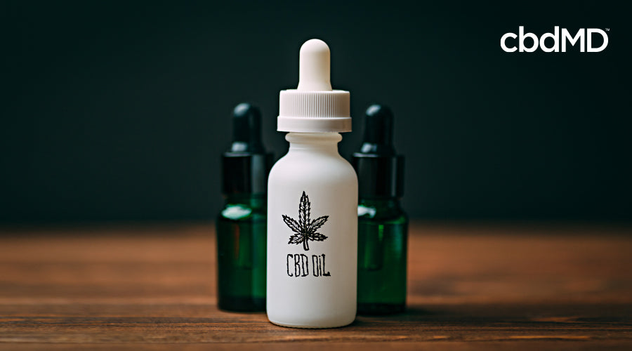 A white bottle labeled cbd oil sits next to two green glass bottles