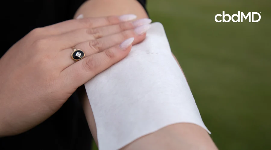 Woman with manicured nails applies a CBD transdermal patch to left arm