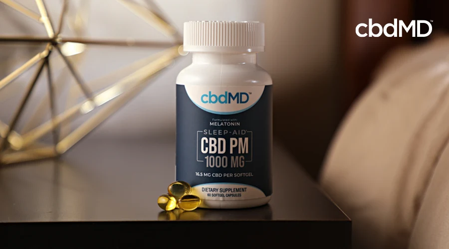 A bottle of 1000 mg cbd pm from cbdmd sits next to a small stack of pills on a nightstand