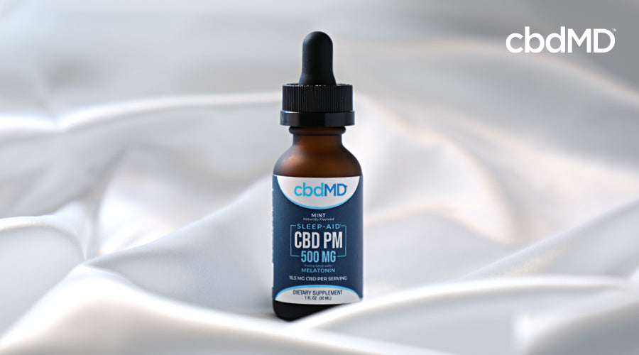 A bottle of 500 mg cbd pm from cbdmd sits among silk sheets