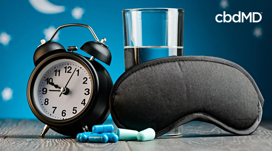 A traditional alarm clock sits alongside cbd pm, a sleep mask, and a glass of water