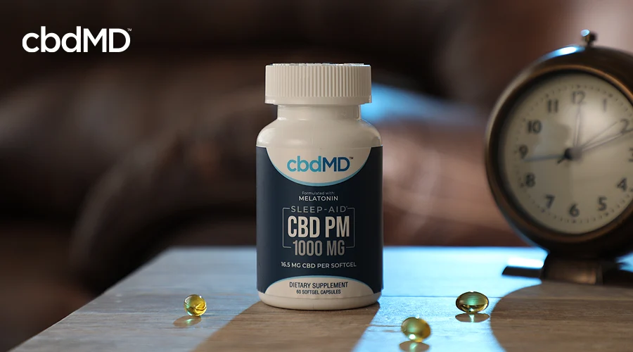 A bottle of cbd pm with melatonin from cbdmd sits on a night stand