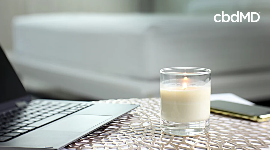 A lit candle sits on a desk next to an open computer