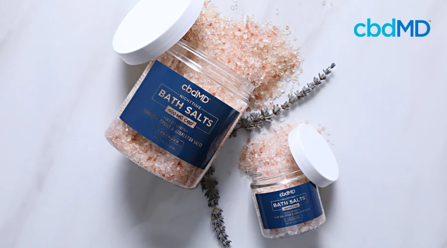 Two different size bottles of cbd bath salts from cbdmd lay on their side with contents spilling out