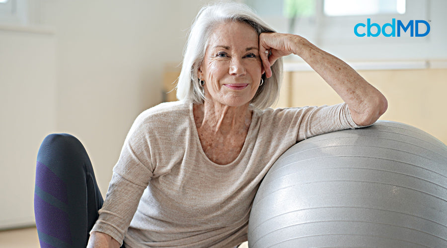 An older woman in workout clothes sits against an exercise ball