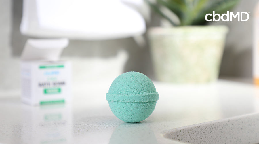 A light blue cbd bath bomb from cbdmd sits on a bathroom countertop