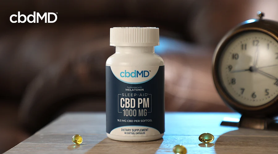 A bottle of 1000 mg cbd pm from cbdmd sits on a beside nightstand near an old fashioned clock