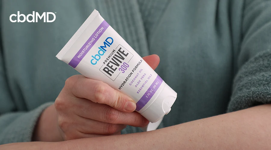 A woman in a bathrobe applies 300 mg cbd revive from a tube