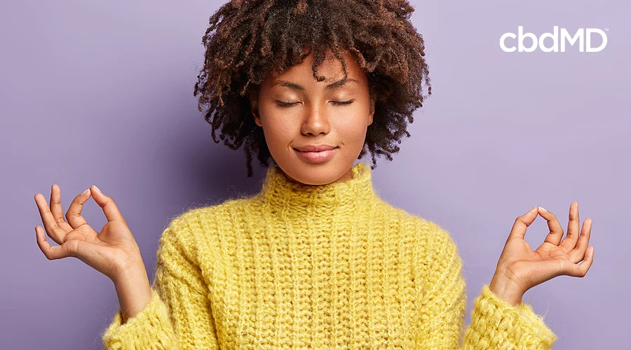 An attractive woman with dark skin and natural hair holds her fingers up together in a meditation pose