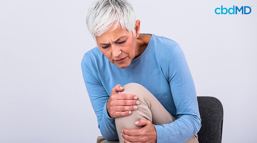 A woman sitting in a chair with pain holding her knee - cbdMD