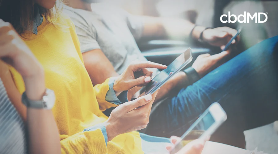 A group of people sit in a row all looking at and playing with their smart phones