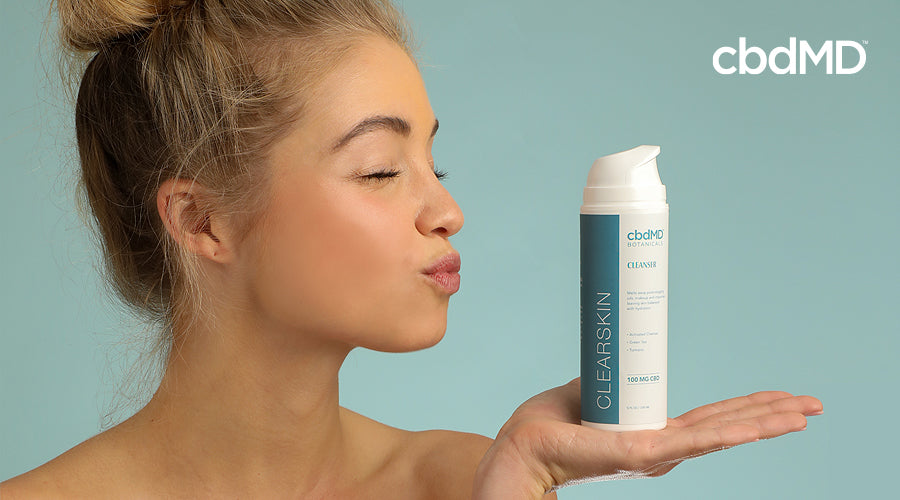 A woman blows a kiss at a bottle of cbd skin care product from cbdmd botanicals