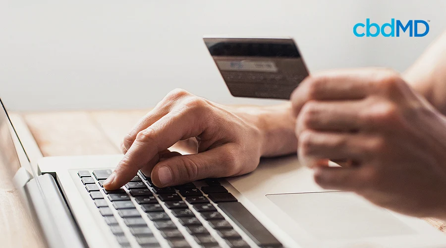 A computer sits on a desktop with someone making a purchase as they hold their credit card