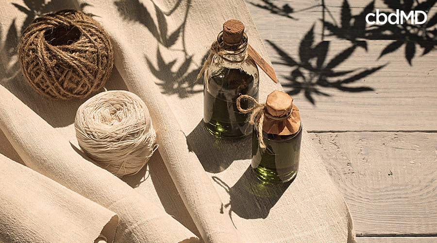 Bottles full of hemp oil next to hemp rope and hemp paper with a shadow of a hemp plant above it - cbdMD