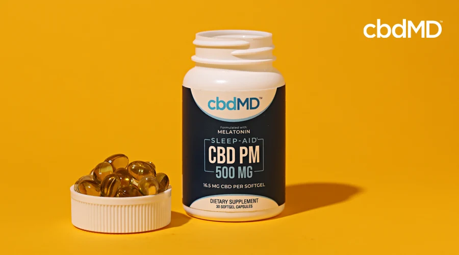A bottle of 500 mg cbd pm softgell capsules sits next to a cap full of capsules