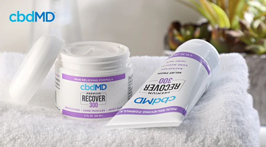 An open jar of 300 mg cbd recover sits on a towel next to a tube of 300 mg recover