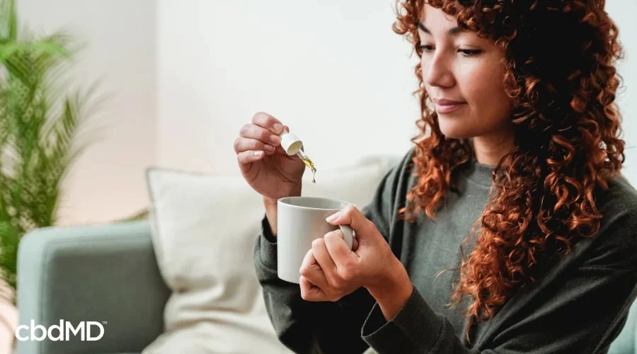 Woman Adding CBD Oil Tincture to Tea to Help with Natural Pain Relief