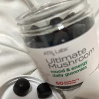 Customer-uploaded image. Click to see more details. The image represents: A bottle of Ultimate Mushroom mood and energy daily gummies with 60 apple berry flavored gummies, shown with two black gummies displayed on a white surface next to the open jar.