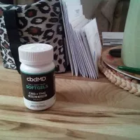 Customer-uploaded image. Click to see more details. The image represents: A bottle of CBD softgels sits on a wooden surface next to a leopard print bag, stack of papers, and woven basket