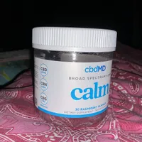 Customer-uploaded image. Click to see more details. The image represents: A white jar of cbdMD Calm gummies containing CBD, CBN, and CBG, sitting on a patterned fabric surface