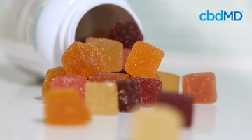 Assorted hemp gummies spilling from a white bottle, close-up view