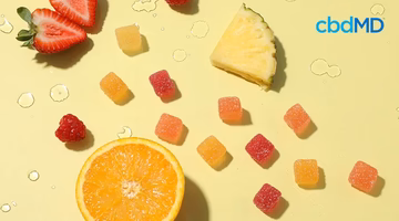 Assorted fruit-flavored hemp gummies with fresh strawberry, orange, raspberry, and pineapple on yellow background