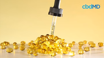 CBD oil dropper and golden CBD capsules on a yellow background, measuring marks visible.