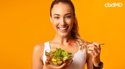Smiling woman eating fresh salad with greens and tomatoes against vibrant yellow background