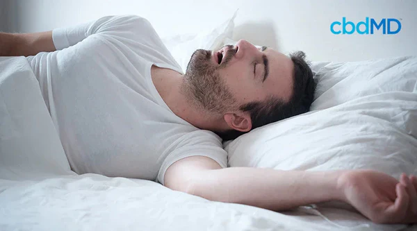 Man in white shirt snoring on bed, illustrating sleep issues and wellness solutions
