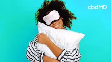 Smiling woman in pajamas and sleep mask hugging pillow on turquoise background