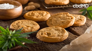 Freshly baked cookies on a wooden surface with green leaves and baking ingredients nearby