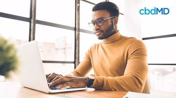 Focused man wearing glasses working on laptop in bright office setting