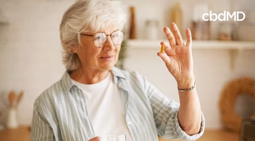 Senior woman holding CBD supplement capsule and glass of water in bright kitchen