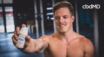 Athlete holding cbdMD Recover cream in gym, sports recovery wellness product