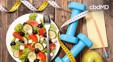 Fresh vegetable salad, blue dumbbells, measuring tape, notepad, and apple on wooden table for healthy lifestyle