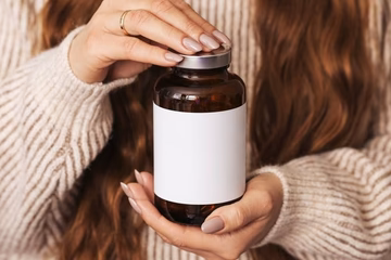 close-up of woman holding a brown supplement bottle with a blank, white label