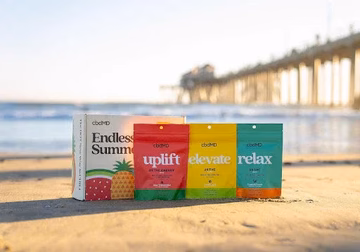 cbdMD wellness gummies and supplement packs on sandy beach near ocean and pier