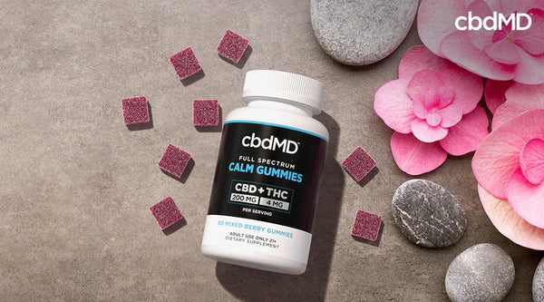 CBD calm gummies bottle with berry gummies, pink flowers, and stones on a neutral background