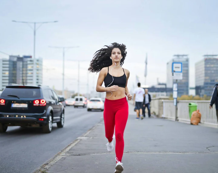 Woman running in city, wearing sportswear and earphones, urban fitness lifestyle