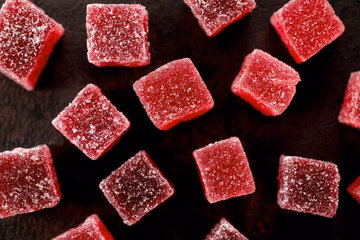 Red sugar-coated gummies arranged on a dark surface, close-up view