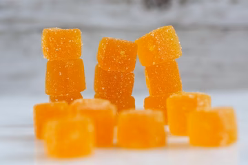 Orange sugar-coated CBD gummies stacked on a white surface